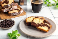 2 Stück Marmorkuchen auf einem Teller, daneben eine Schale Schokodrops, der angeschnittene Kastenkuchen auf einem Brett und eine Tasse Kaffee.
