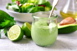 Ein Glas Avocado-Joghurt-Dressing mit Löffel, drumherum je eine halbierte Limette und Avocado.