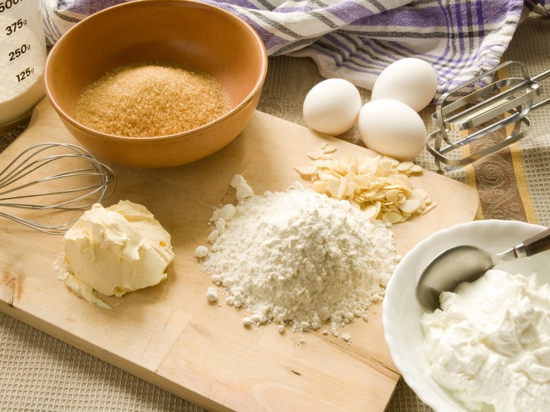 Backmischung aufpeppen: Backutensilien wie Mehl, Butter, Zucker und Eier sowie Rührstäbe eines Handmixers. Nahaufnahme.