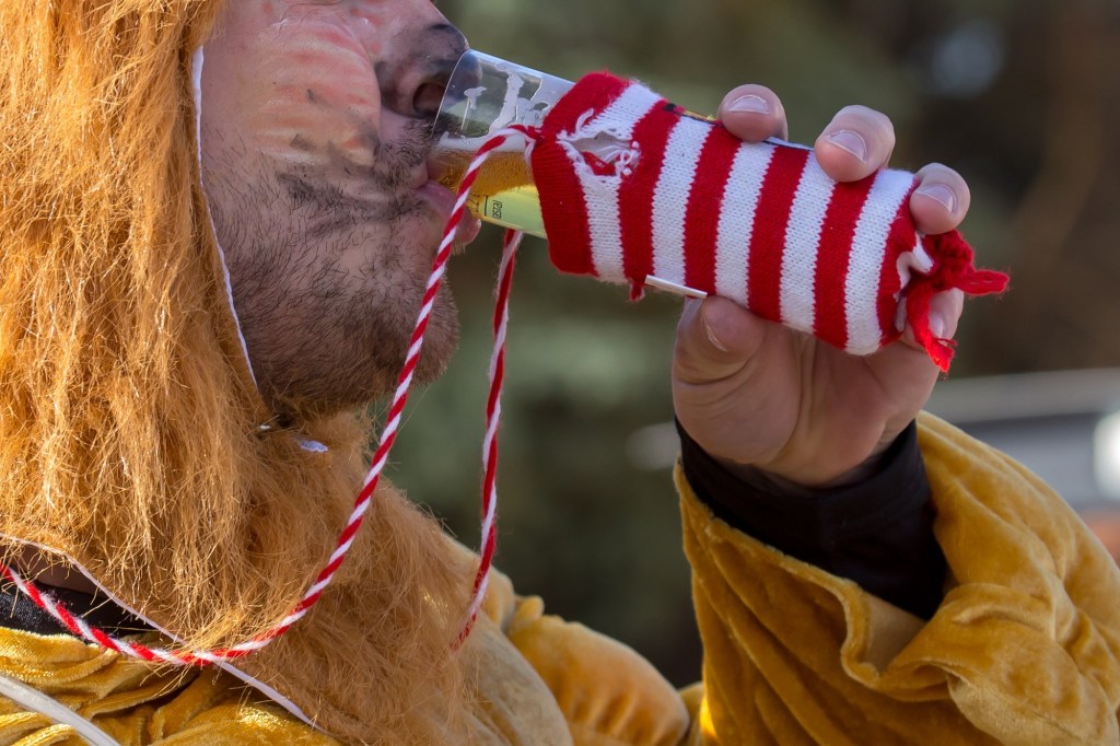 Ein Besucher des Kölner Karnevals im Löwenkostüm trägt sein Kölsch um den Hals