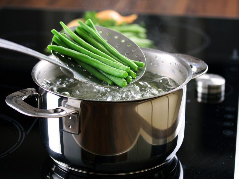 Grüne Bohnen werden nach dem Blanchieren aus dem kochenden Wasser genommen.