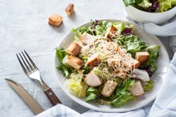 Teller mit Caesar Salat und Besteck auf hellem Untergrund