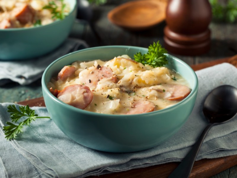 Eine Schüssel cremige Sauerkrautsuppe mit Würstchen und Petersilie.