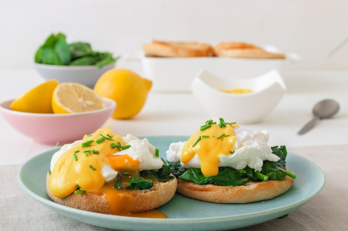 Eggs Florentine aus Spinat mit Käsesoße auf einem blauen Teller.