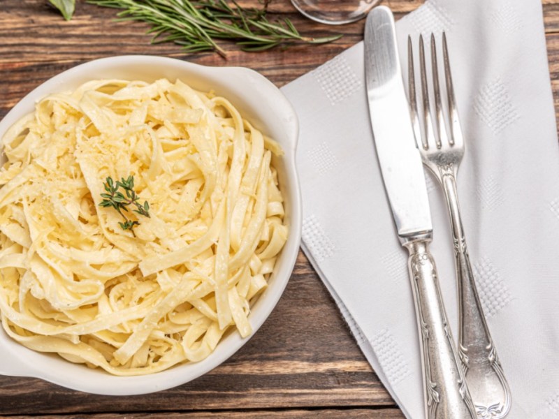 Eine Portion Fettucine Alfredo. Daneben liegt Besteck auf einer Serviette.