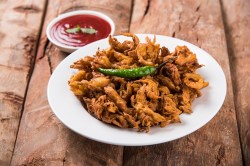 Indische Gemüsekrapfen auf einem weißen Teller, dekoriert mit einer grünen Chili und serviert mit einer roten Soße.