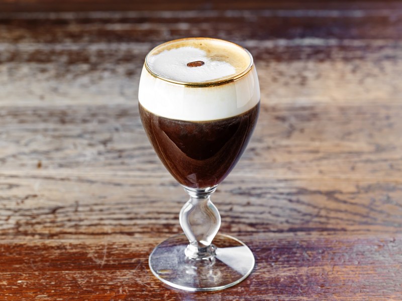 Ein Glas Irish Coffee auf einem Holztisch, garniert mit einerKaffeebohne.