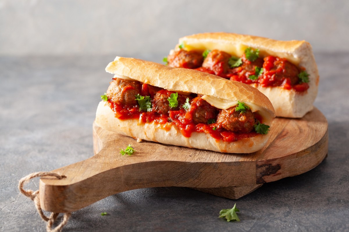2 Italienische Meatball-Sandwiches mit Käse und Petersilie und Tomatensoße auf einem Brett.