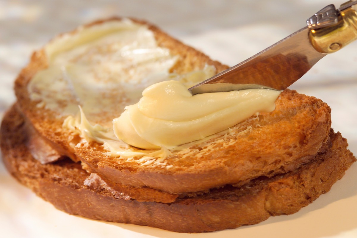 Butter wird mit einem Messer auf eine Brotscheibe geschmiert.