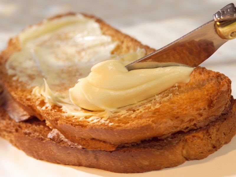 Butter wird mit einem Messer auf eine Brotscheibe geschmiert.
