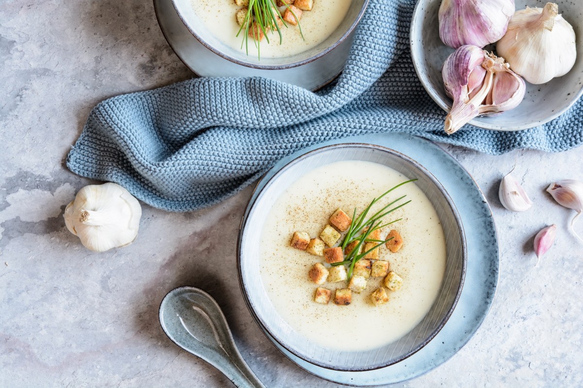 Schale Knoblauchsuppe mit Coutons auf einem Tisch mit blauem Tischtuch.