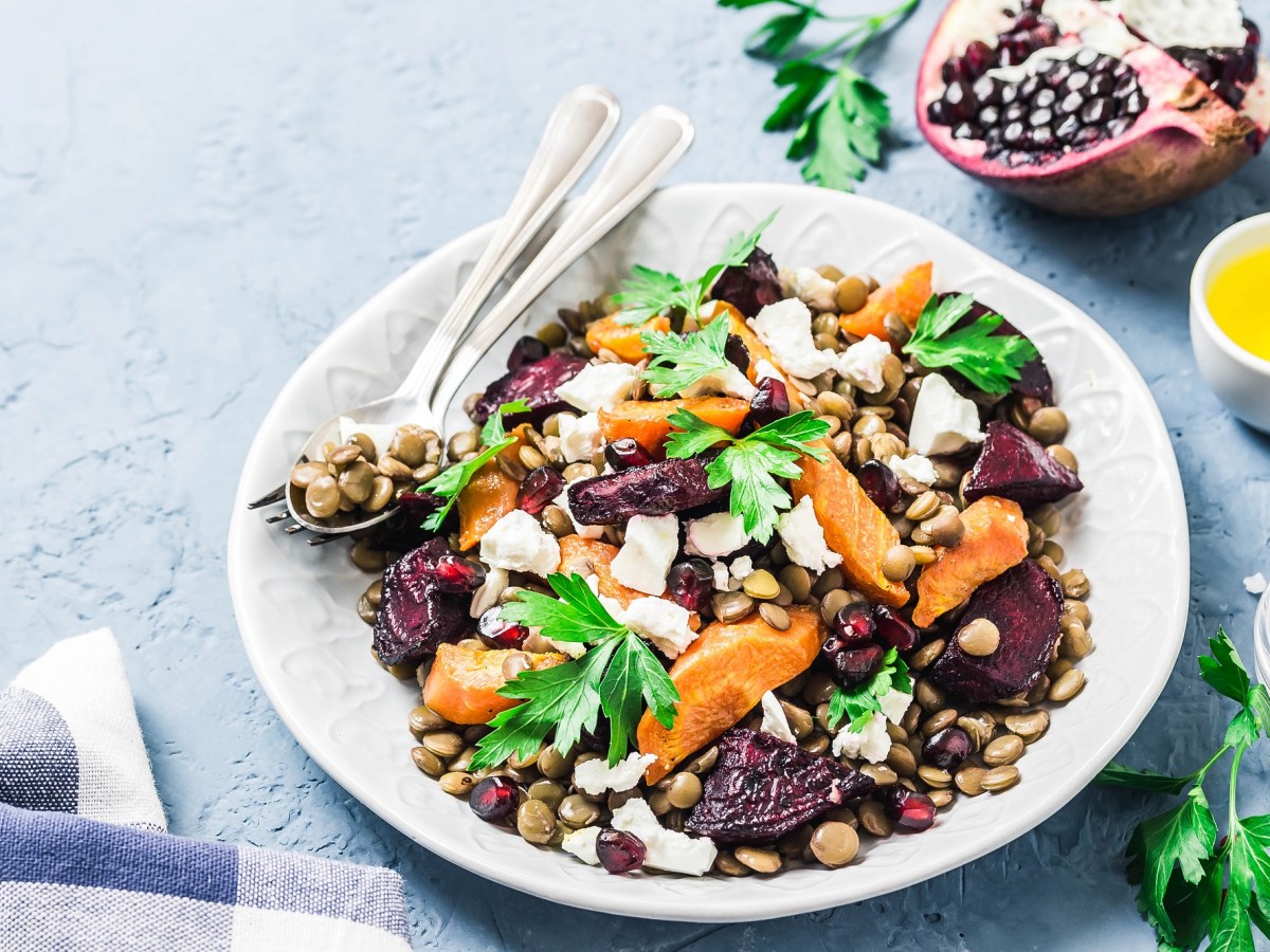 Linsensalat mit Wintergemüse auf einem weißen Teller. Daneben Petersilie und eine Schale Olivenöl.