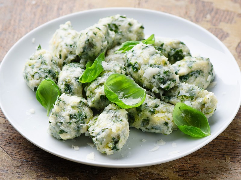 Malfatti mit Spinat und Ricotta auf einem weißen Teller, mit Basilikum garniert.