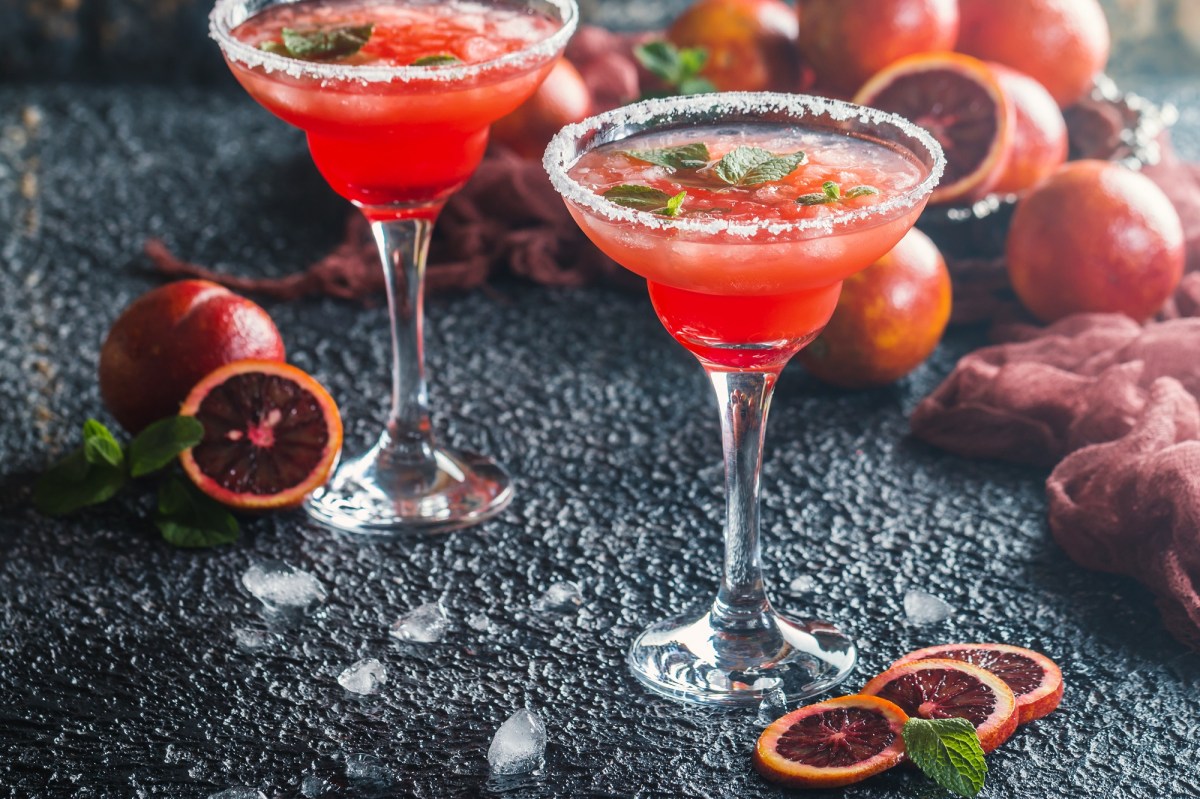 Zwei Gläser mit rotem Cocktail und Blutorangen auf einem Tisch.