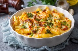 Nudelauflauf mit Brokkoli und Gorgonzola in einer weißen Auflaufform auf einem blauen Tuch.