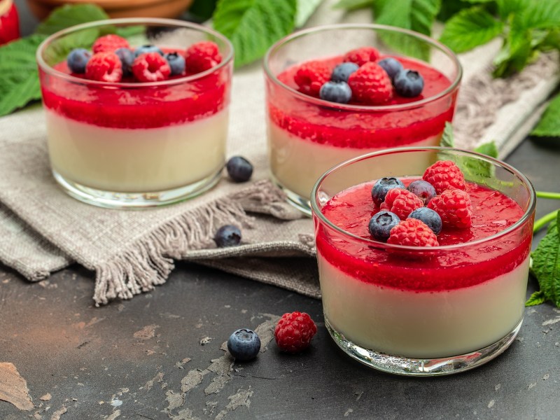 Panna Cotta mit Beerensoße und frischen Beeren garniert in kleinen Gläsern.