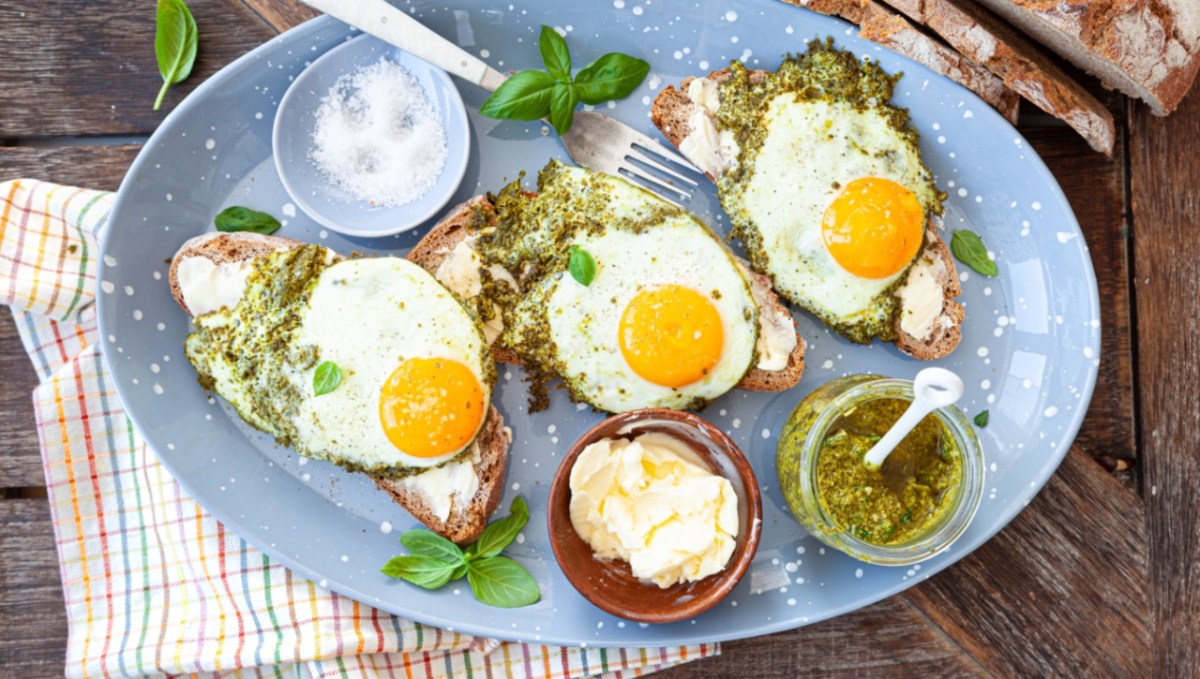 Drei Pesto-Eier auf Brotscheiben. Drumherum stehen Schalen mit Pesto, Butter und Salz.