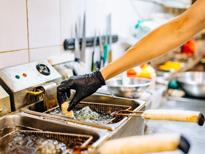 Ratgeber zum richtigen Frittieren: Eine Hand legt ein Stück Frittiergut in eine Fritteuse