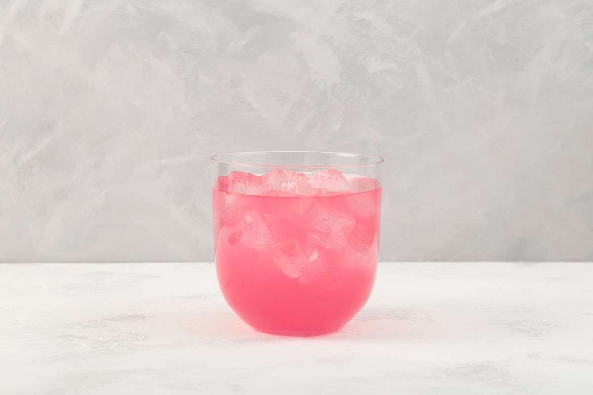 Ein Glas Sarti Spritz mit Eiswürfeln vor grauem Hintergrund