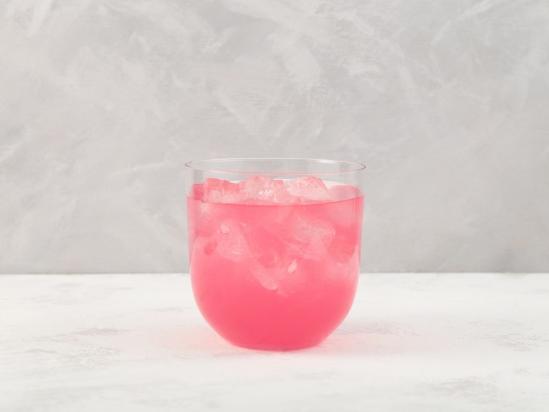Ein Glas Sarti Spritz mit Eiswürfeln vor grauem Hintergrund
