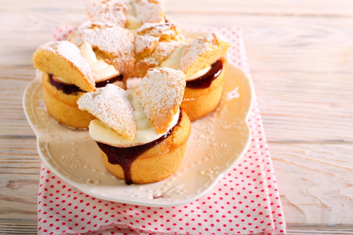 Mehrere Schmetterling-Cupcakes mit Creme und Marmelade auf einem Teller, der auf einem Geschirrtuch steht.