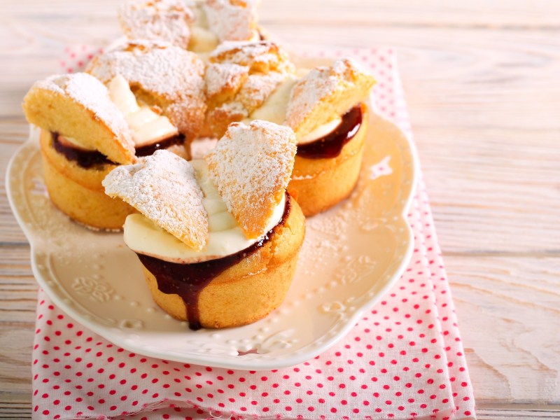 Mehrere Schmetterling-Cupcakes mit Creme und Marmelade auf einem Teller, der auf einem Geschirrtuch steht.