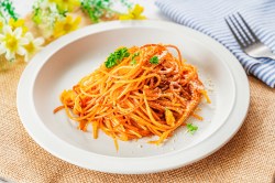 Spaghetti all'Assassina auf einem weißen Teller, daneben liegt eine Gabel.