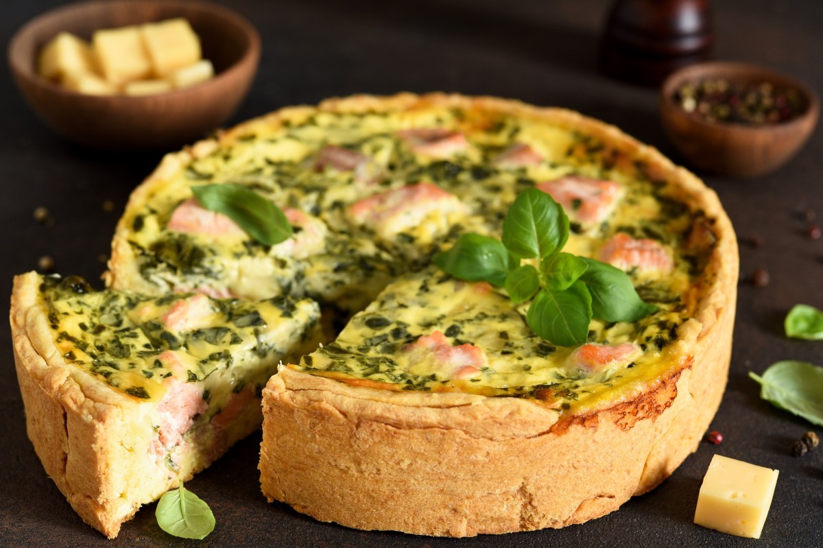 Spinat-Lachs-Quiche mit Basilikum dekoriert auf einem dunklen Untergrund.