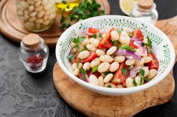 Schale mit Salat, weiße Bohnen, Tomaten und Zwiebeln auf einem Tisch.