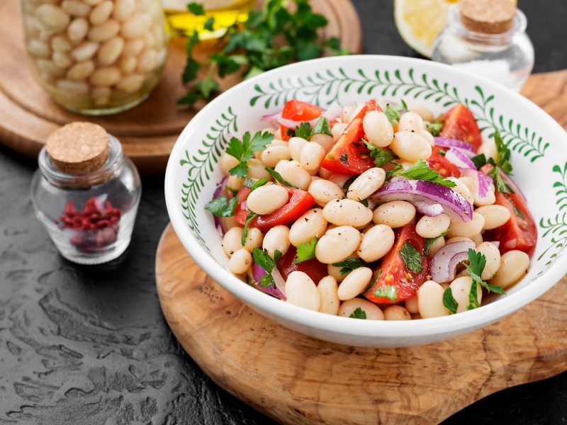 Schale mit Salat, weiße Bohnen, Tomaten und Zwiebeln auf einem Tisch.