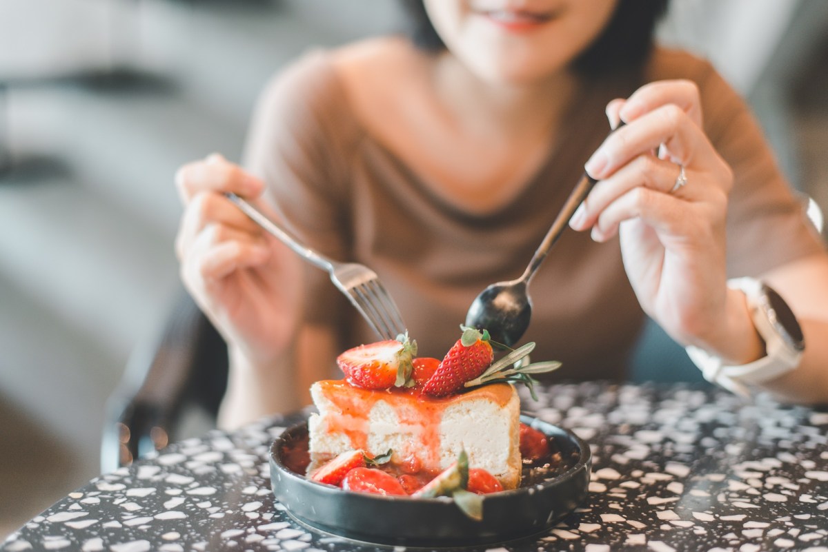 Unterschied Käsekuchen und Cheesecake: Eine Frau isst ein Stück Cheesecake mit Erdbeeren.