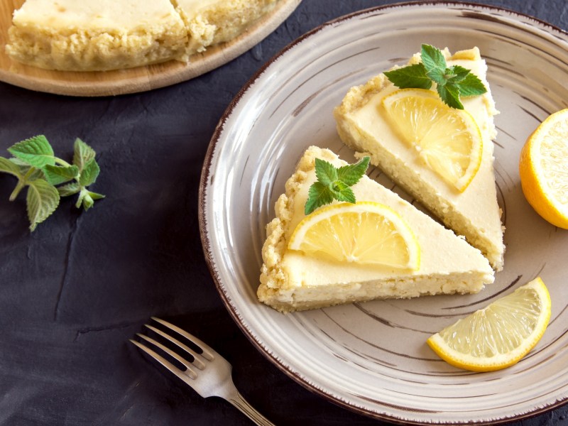 Teller mit zwei Stücken Zitronen-Cheesecake auf dunklem Untergrund