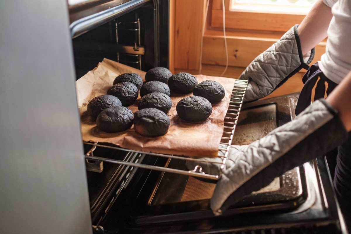 Angebranntes Essen: Eine Person mit Ofenhandschuhen holt verbrannte Brötchen aus einem Ofen.