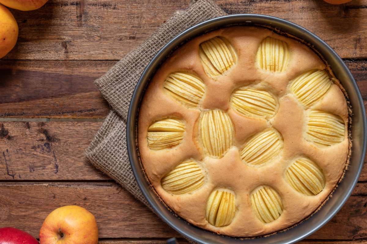 Ein Apfelkuchen ohne Zucker in der Backform von oben fotografiert. Es liegen frische Äpfel daneben.