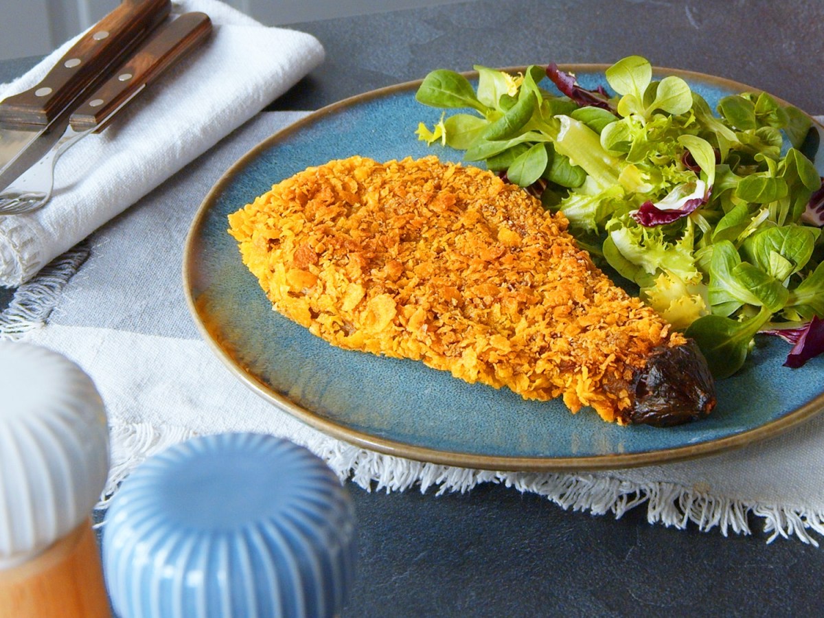 Ein Teller mit Auberginenschnitzel und Salat auf einem blau-weißen Tischtuch mit Salz- und Pfefferstreuer.