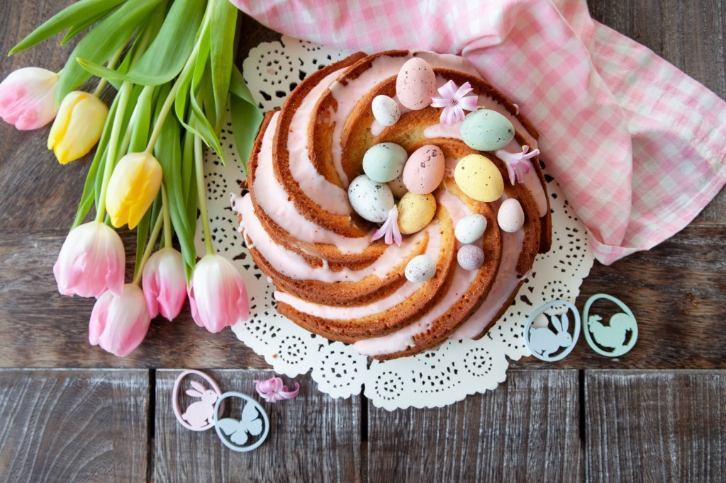Babka Wielkanocna, polnischer Osterkuchen in Gugelhupf-Form, verziert mit Zuckereiern und Zuckerguss, Draufsicht, daneben Tulpen.