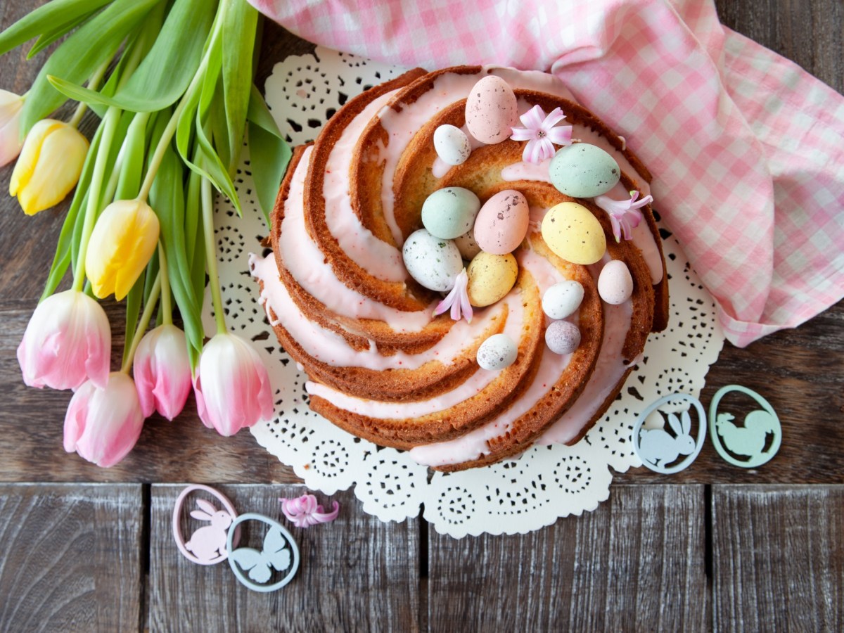 Babka Wielkanocna, polnischer Osterkuchen in Gugelhupf-Form, verziert mit Zuckereiern und Zuckerguss, Draufsicht, daneben Tulpen.