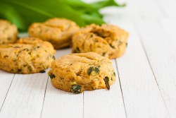 Mehrere Bärlauch-Scones auf weißem Holz, dahinter unscharf frischer Bärlauch.