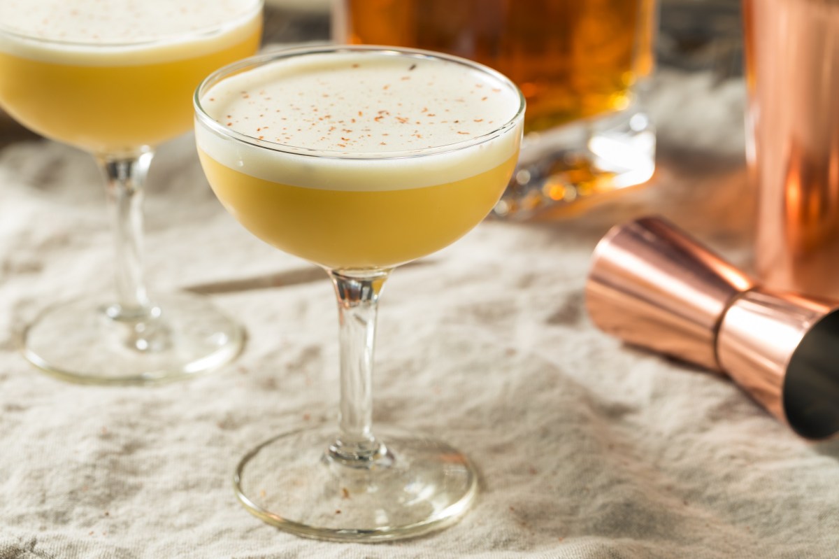 Zwei Gläser Bourbon Flip Cocktail mit Cocktailshaker auf hellem Tischtuch.