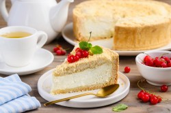 Ein Stück Dreh-dich-um-Kuchen, garniert mit Johannisbeeren und Minze, auf einem weißen Teller, Daneben liegt ein goldener Löffel. Im Hintergrund unscharf der Rest des Kuchens.