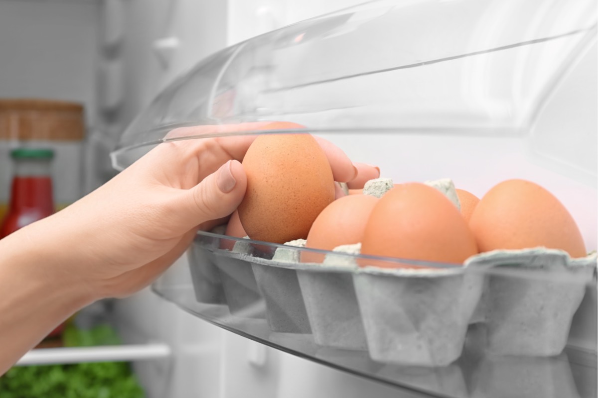 Eine Frau entnimmt ein Ei aus einer Eierpackung, die in der Kühlschranktür gelagert wird.