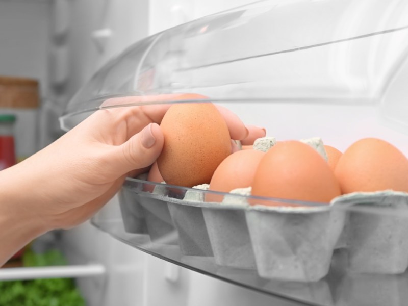 Eine Frau entnimmt ein Ei aus einer Eierpackung, die in der Kühlschranktür gelagert wird.