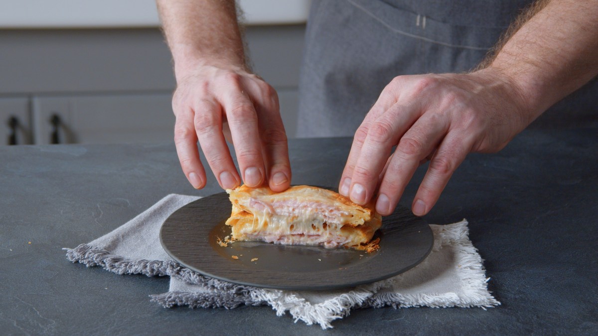 Käse-Schinken-Toasties aus Blätterteig auf einem Teller, männliche Hände drücken sie zusammen.