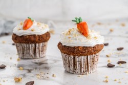 2 Karottenkuchen-Cupcakes, mit Marzipanmöhren dekoriert.