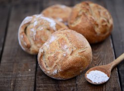 selbst gebackene Kartoffel-Brötchen mit Löffel Mehl auf Holztisch