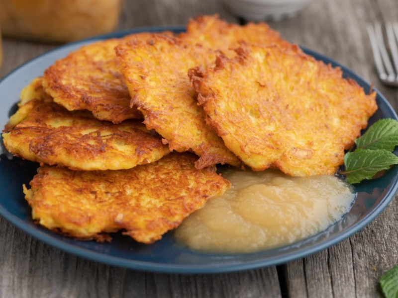 Mehrere Kartoffelpuffer mit Apfelmus auf einem Teller. Daneben liegt eine Gabel.