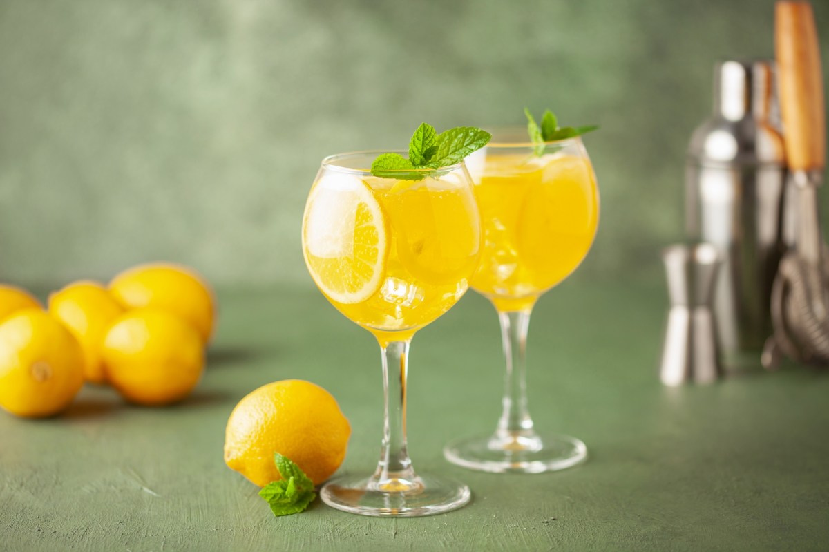2 Gläser Limoncello Spritz mit Eiswürfeln, Zitronenscheiben und Minze. Dahinter Zitronen und ein Cocktailshaker.