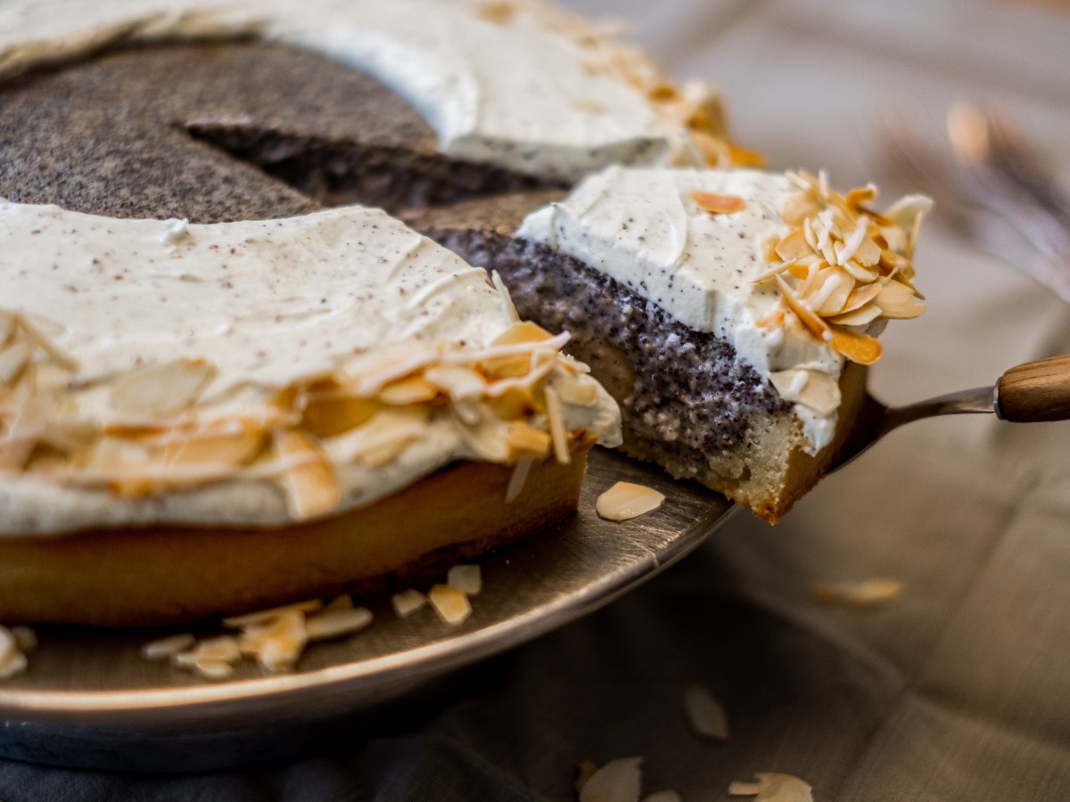 Mohnkuchen mit Birnen und Quark sowie Mandeln, aus dem ein Stück mit einem Tortenheber herausgenommen wird.