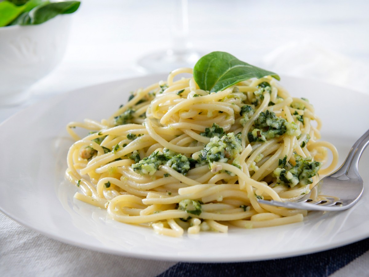 Ein Teller Ofen-Spaghetti mit Spinat und Feta, garniert mit einem Basilikumblatt, auf dem Teller auch eine Gabel.