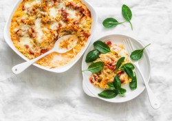 Eine Auflaufform mit Orzo-Feta-Auflauf mit Tomaten, daneben ein Teller mit etwas Auflauf und frischem Spinat.